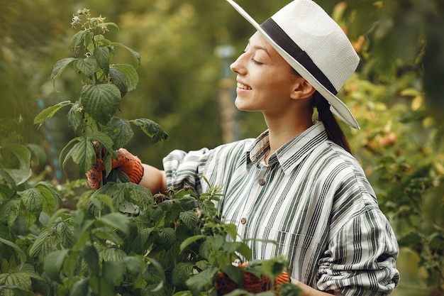 Young woman taking care of plants. Brunette in a hat and gloves.