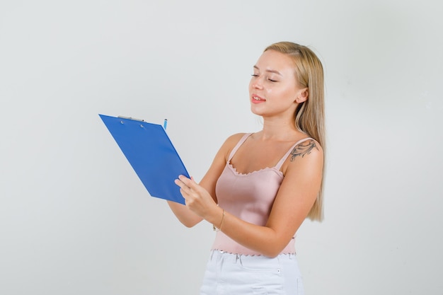 Young woman taking notes on clipboard in singlet, mini skirt and looking busy.