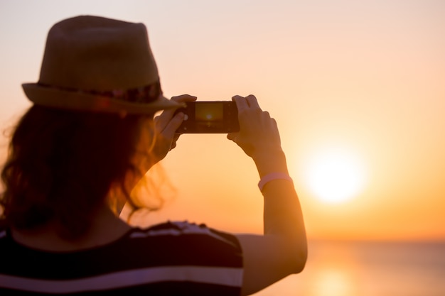 Young woman taking photo of sea sunset