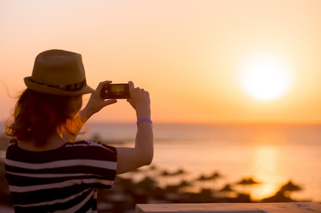 Free photo young woman taking picture of sea sunrise