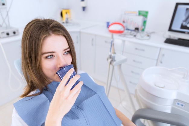 Young woman taking water while sitting in dental chair