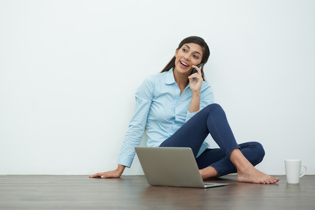 Young Woman Talking on Phone on Floor with Laptop