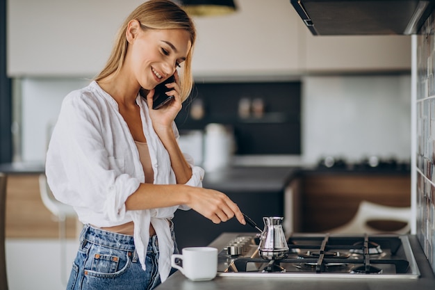 Free Photo young woman talking on the phone and making morning coffee