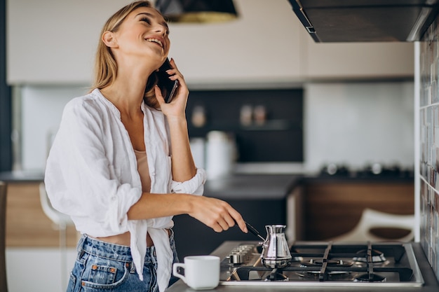 Young woman talking on the phone and making morning coffee