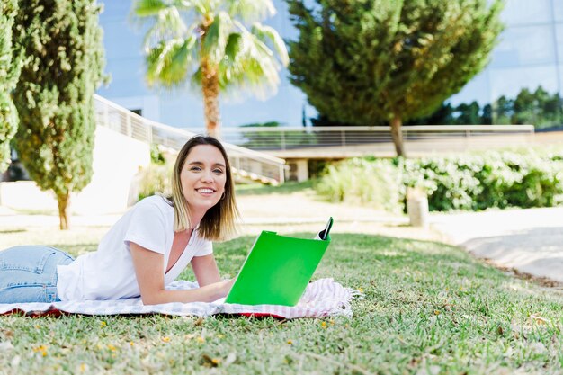 Young woman textbook lying on park ground