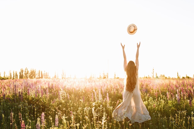 Free photo young woman throw up straw hat in flower field on sunset.