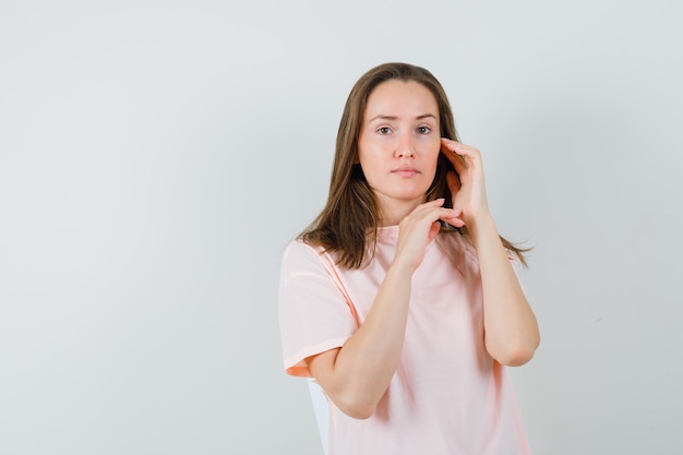 Young woman touching face skin on cheek in pink t-shirt and looking delicate.