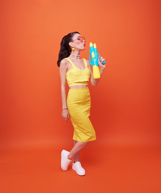 Free photo young woman tourist happy with water gun during songkran festival holiday on orange background