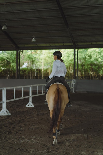 Free photo young woman trains in horseback riding in the arena. young caucasian woman in formal clothing horseback riding across the sandy arena. a pedigree horse for equestrian sport. the sportswoman on a horse