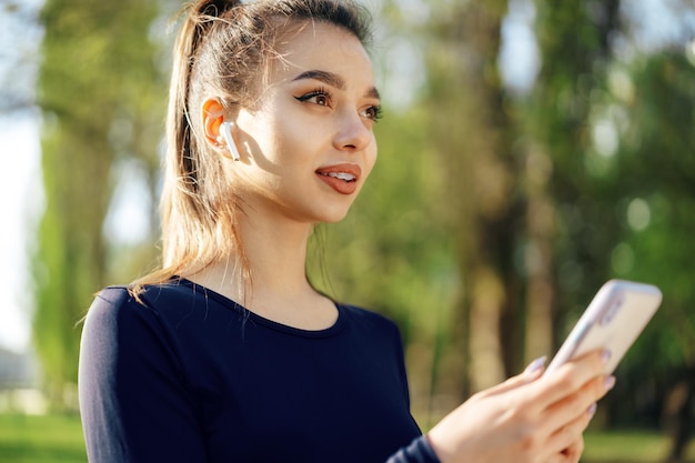 Free photo young woman turns on music for running on her smartphone outdoors