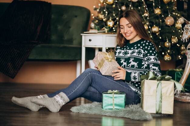 Young woman unpacking christmas present by the christmas tree