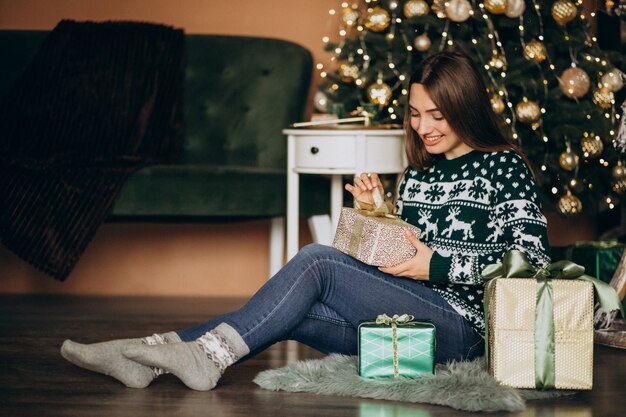 Young woman unpacking christmas present by the christmas tree