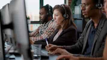 Free photo young woman using audio headset and computer at call center job, offering helpline assistance to people. female consultant talking to clients at customer care service, helping with telemarketing.