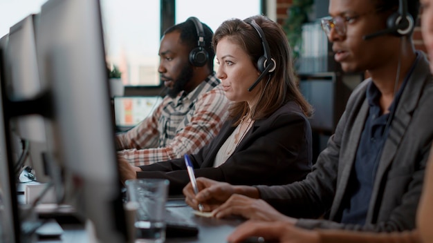 Young woman using audio headset and computer at call center job, offering helpline assistance to people. Female consultant talking to clients at customer care service, helping with telemarketing.