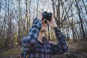 Free photo young woman using binoculars in the forest