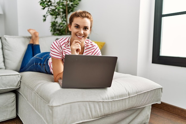 Free photo young woman using laptop lying on sofa at home