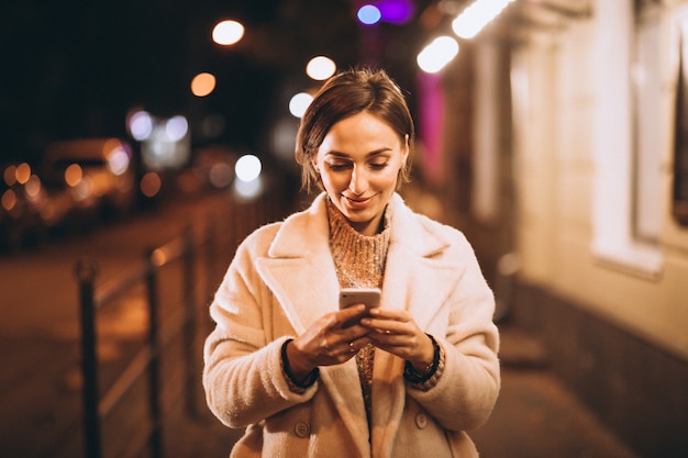 Free photo young woman using phone outside the night street