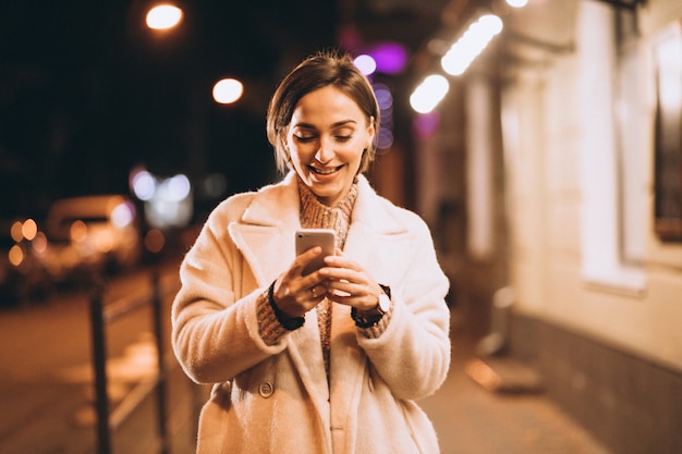 Free photo young woman using phone outside the night street