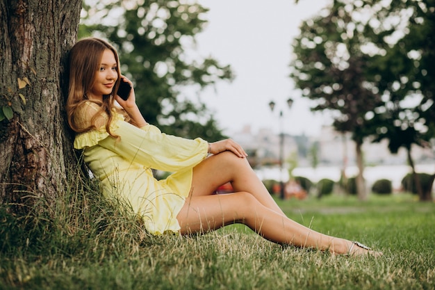 Young woman using phone, and sitting under the tree in park