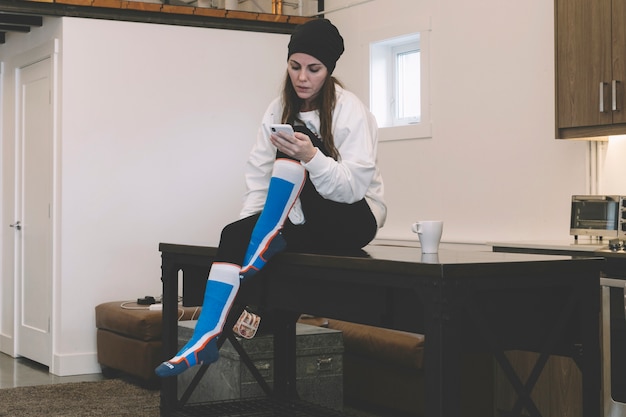 Young woman using smartphone on kitchen table 