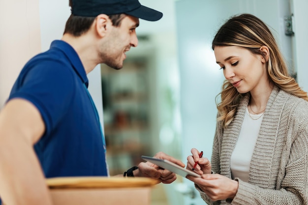 Free photo young woman using touchpad to sign for package delivery from a courier while standing on a doorway