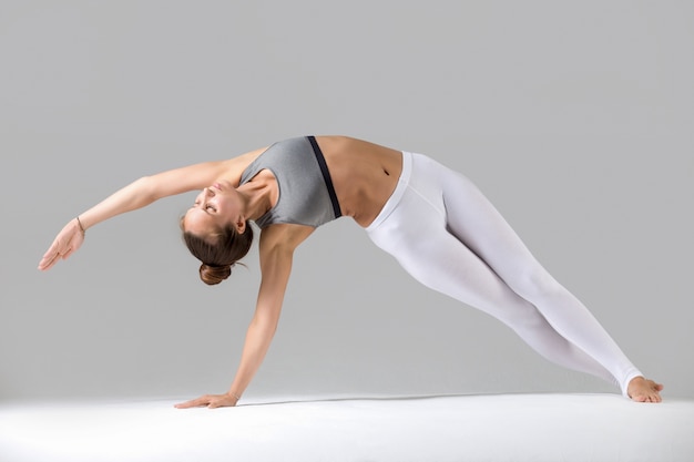 Young woman in Vasisthasana pose, grey studio background