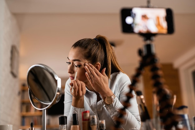 Free photo young woman vlogging about beauty products while applying eyeshadow at home