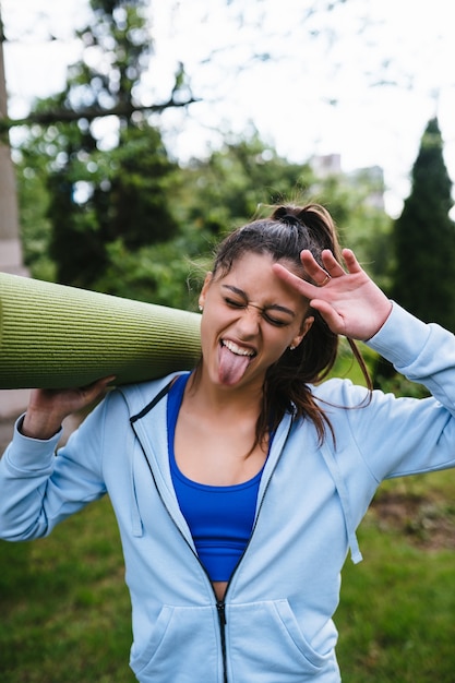 Young woman walking in urban park holding fitness rug.