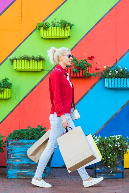 Free photo young woman walking with bags near wall