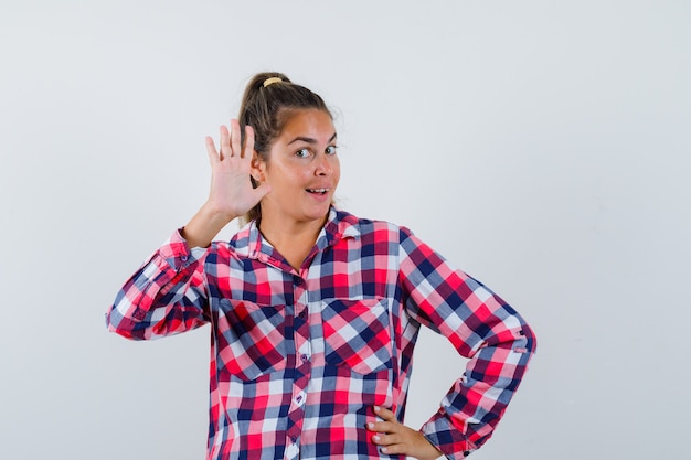 Young woman waving hand to say goodbye in casual shirt and looking happy. front view.