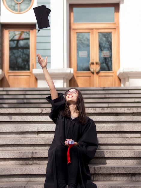 Free photo young woman wearing graduation gown in front of university