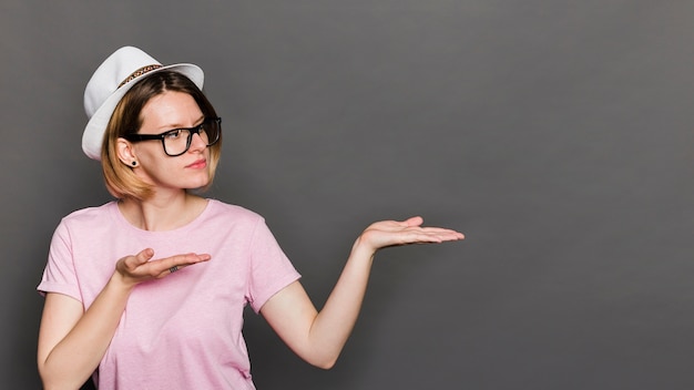 Free photo young woman wearing hat presenting something against grey background