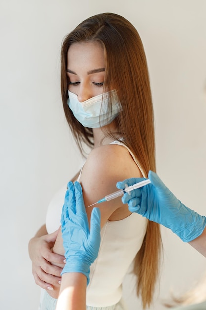 Free Photo young woman wearing mask and receiving coronavirus vaccine a young girl receiving an immunity shot in the forearm closeup of doctor in blue gloves giving covid19 aids