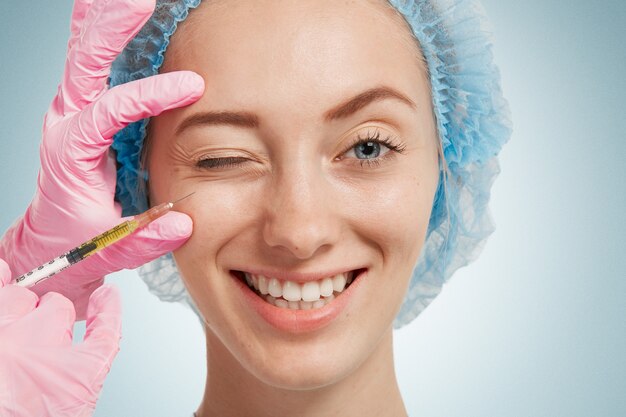 Young woman wearing medical headwear while doctor injects her face