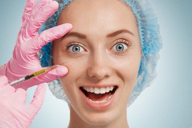 Young woman wearing medical headwear while doctor injects her face