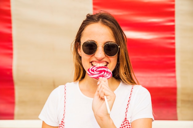 Free photo young woman wearing sunglasses biting lollipop