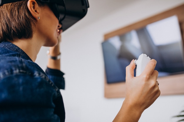 Free photo young woman wearing vr glasses and playing virtual game using remote