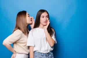 Free photo young woman whispers to her mate bad news isolated on blue wall