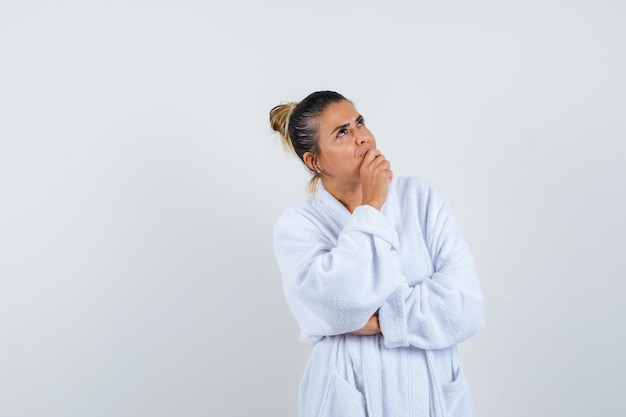 Free photo young woman in white bathrobe standing in thinking pose and looking pensive