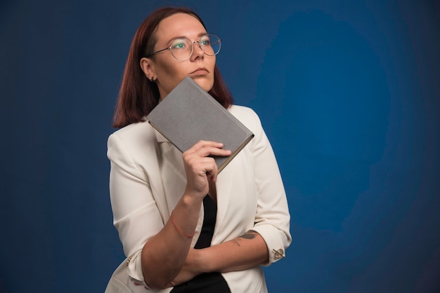 Young woman in white blazer holding a book and thinking.