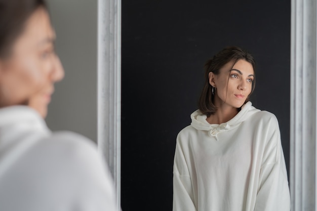 Free photo young woman in white hoodie posing in the mirror