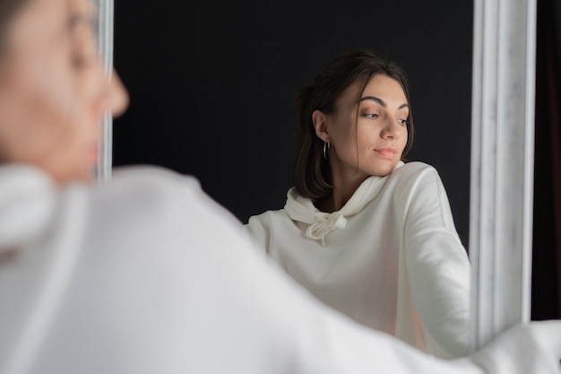 Young woman in white hoodie posing in the mirror