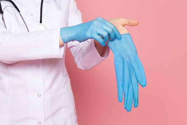 young woman in white medical suit blue gloves blue protective mask with stethoscope on pink