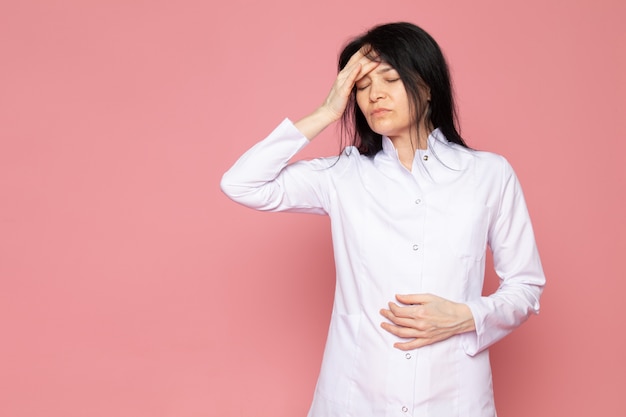 young woman in white medical suit having a severe headache on pink