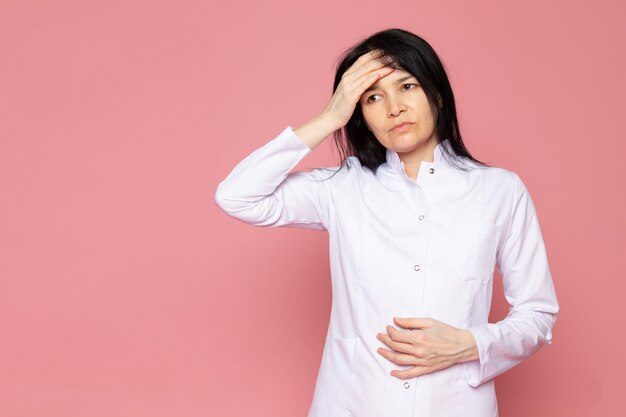 young woman in white medical suit having a severe headache on pink