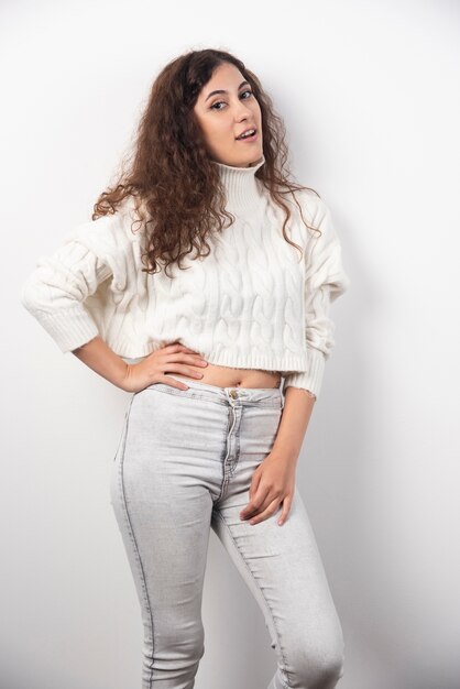 Young woman in white sweater standing over a white wall. High quality photo