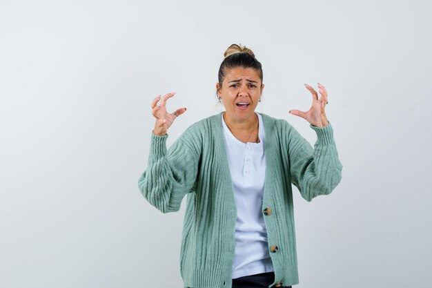 Young woman in white t-shirt and mint green cardigan stretching hands as holding something and looking annoyed