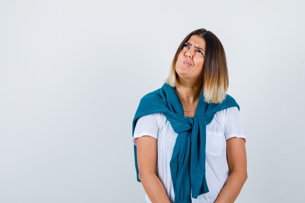 Young woman in white t-shirt twisting mouth to the side and looking wistful , front view.