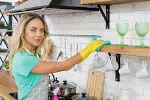 Free photo young woman wiping kitchen shelf looking at camera