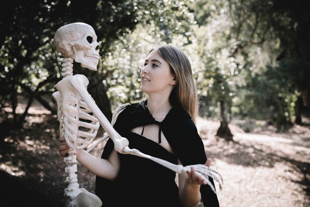 Young woman in witch clothes holding skeleton